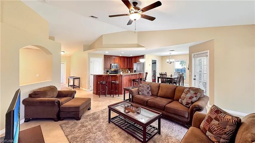 Tiled living room with high vaulted ceiling and ceiling fan with notable chandelier