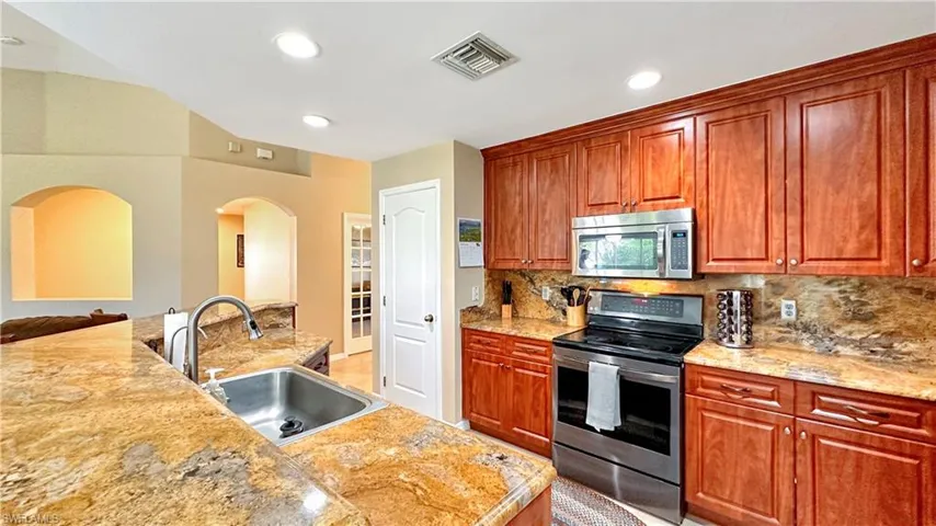 Kitchen featuring backsplash, stainless steel appliances, sink, and light stone countertops