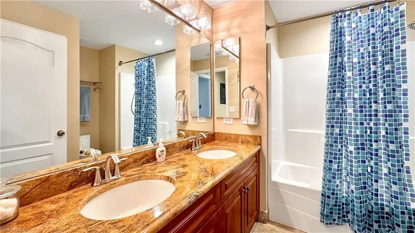 Full bathroom featuring dual vanity, toilet, and shower / bath combo with shower curtain
