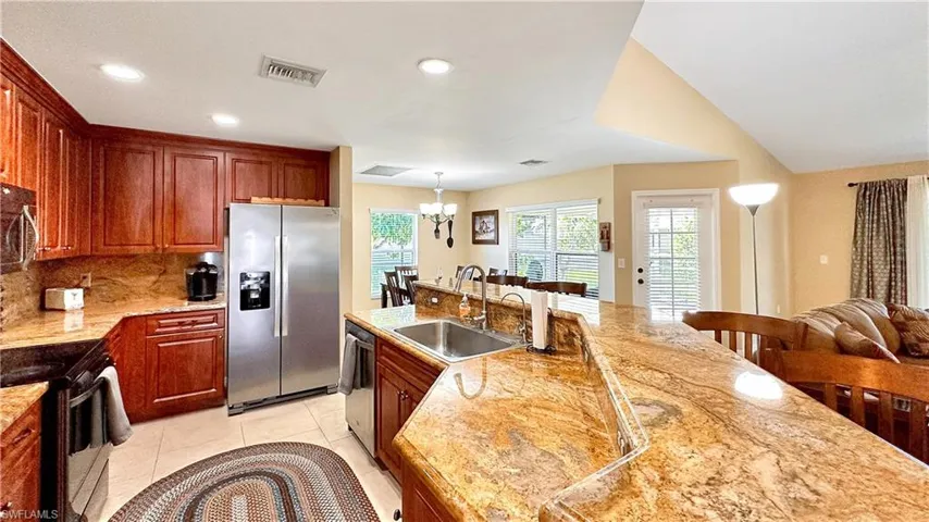Kitchen featuring appliances with stainless steel finishes, a notable chandelier, light tile patterned flooring, tasteful backsplash, and sink