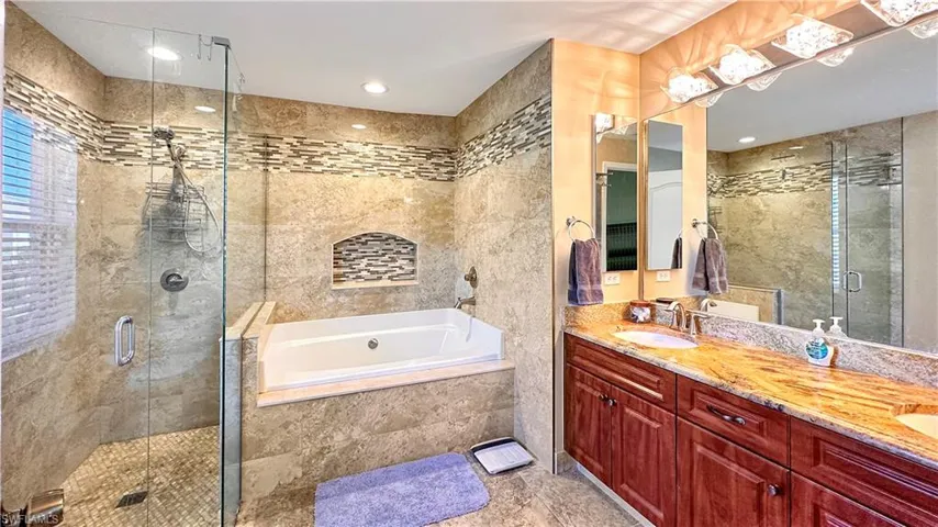 Bathroom with tile walls, dual vanity, tile patterned floors, and independent shower and bath