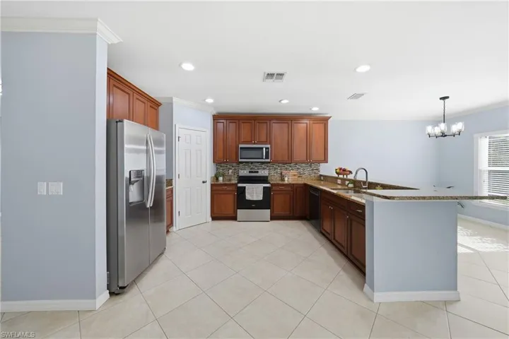 Kitchen featuring stained-wood cabinetry, stone-finish countertops, stainless steel appliances, ceramic tile flooring, and a breakfast bar