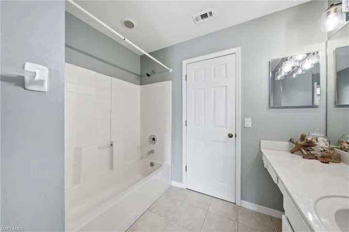 Bathroom featuring a tub and shower combination with white tile surround, vanity with an integrated countertop, wall-mounted mirror, and ceramic tile flooring
