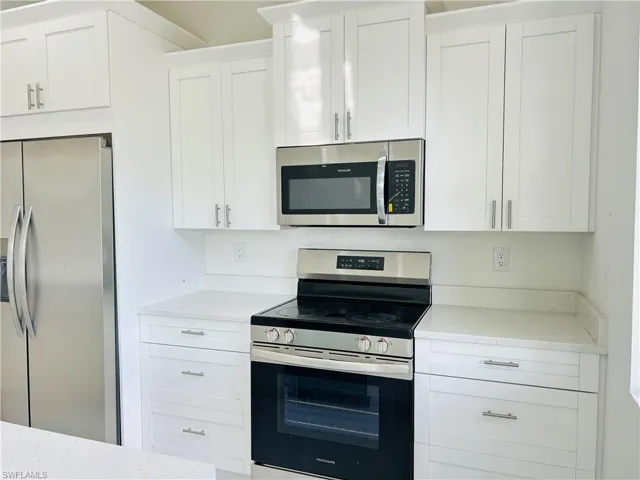 Kitchen with stainless steel appliances, white cabinetry, and light stone countertops