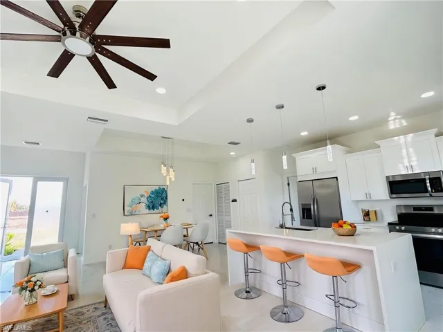Virtually staged kitchen/Living room with open floor plan, stainless steel appliances, white cabinets, an island with sink, and a raised ceiling