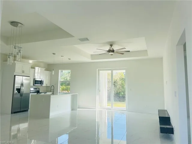 Kitchen with white cabinetry, stainless steel appliances, a tray ceiling, ceiling fan, and a center island with sink