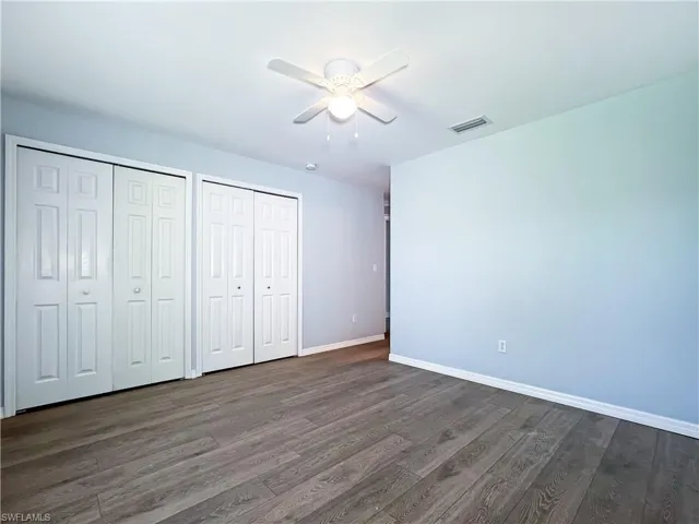 Unfurnished bedroom featuring multiple closets, a ceiling fan, and dark wood-type flooring