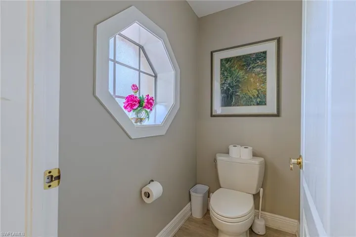Powder room featuring an octagonal window with frosted glass, light neutral wall paint, white trim, and wood-finish flooring