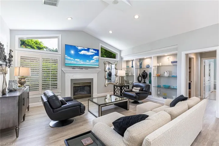 Living area featuring vaulted ceilings, a fireplace with a mantel, built-in shelving with recessed lighting, transom windows, and wood-finish flooring