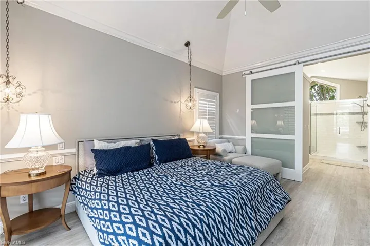 Vaulted ceiling bedroom with light wood-finish flooring, featuring crown molding and a ceiling fan