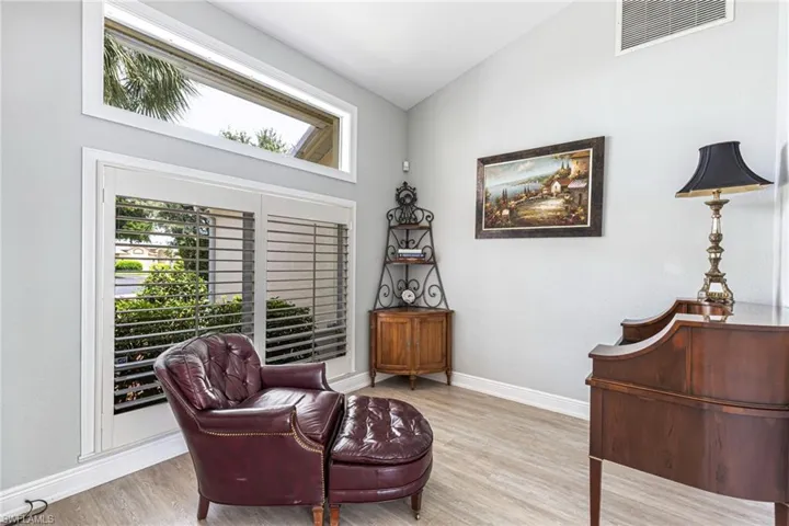 Interior space featuring light gray walls, wood-finish flooring, white baseboards, and a transom window above plantation-shuttered glass doors