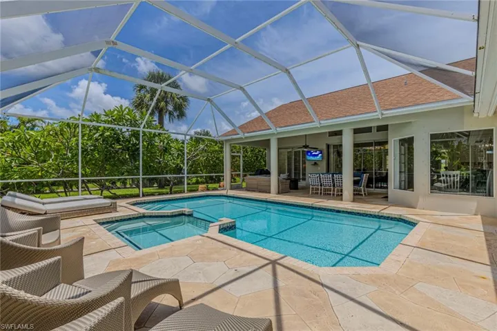 Screened outdoor living area featuring a swimming pool, integrated spa, and expansive patio
