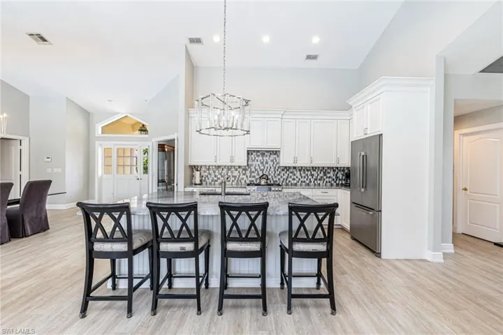 Open-concept kitchen featuring white cabinetry, a gray mosaic tile backsplash, stainless steel appliances, a large island with a breakfast bar, and wood-finish flooring