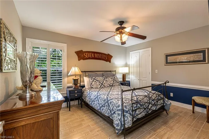 Bedroom featuring light wood-finish flooring, a ceiling fan with integrated lighting, a double-door closet, and white plantation shutters