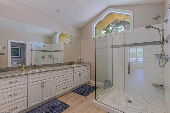 Spacious bathroom featuring a dual vanity with light-toned countertops, a full-width mirror, and extensive white cabinetry