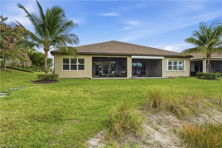 Rear view of property with a lawn, stucco siding, a sunroom, and a tile roof