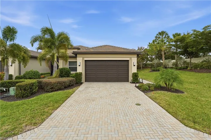 View of front of home with decorative driveway, a front lawn, stucco siding, an attached garage, and a tile roof