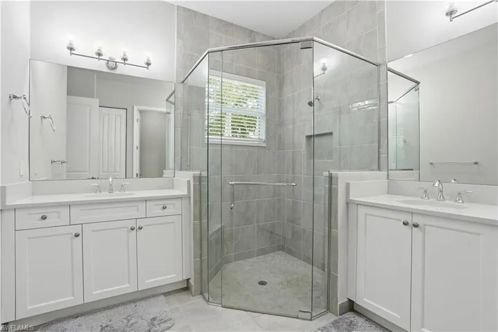Bathroom featuring a stall shower, two vanities, and light tile patterned floors