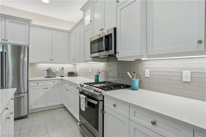 Kitchen featuring appliances with stainless steel finishes, white cabinetry, light tile patterned flooring, and light stone countertops