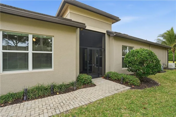 View of exterior entry with stucco siding, a yard, and a sunroom