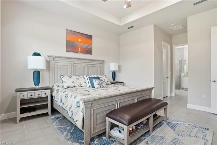 Bedroom featuring ensuite bathroom, light tile patterned floors, and ceiling fan