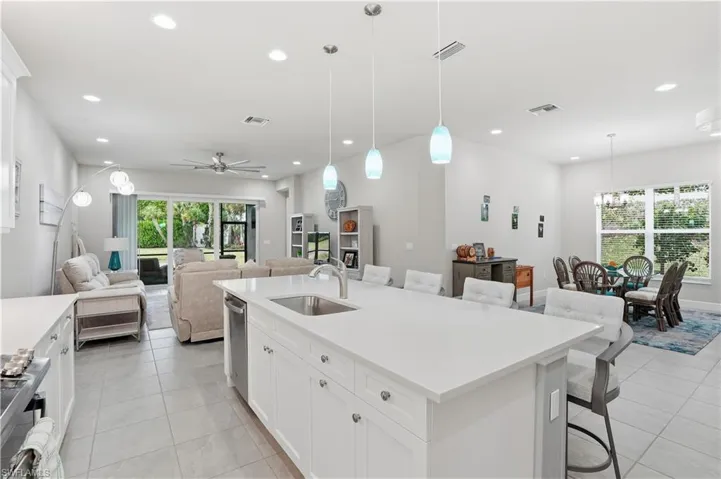 Kitchen featuring white cabinets, a breakfast bar area, hanging light fixtures, an island with sink, and recessed lighting
