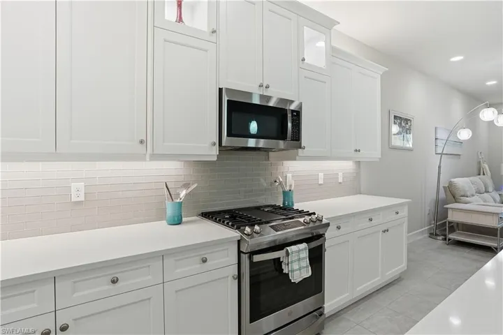 Kitchen featuring stainless steel appliances, white cabinetry, light stone counters, decorative backsplash, and recessed lighting