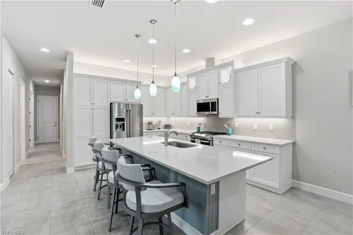 Kitchen with white cabinetry, stainless steel appliances, an island with sink, a kitchen bar, and hanging light fixtures