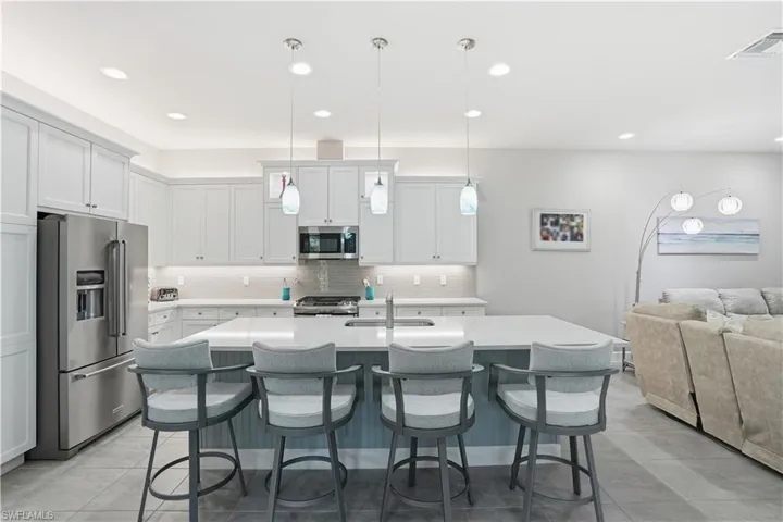 Kitchen featuring appliances with stainless steel finishes, a center island with sink, pendant lighting, open floor plan, and white cabinets