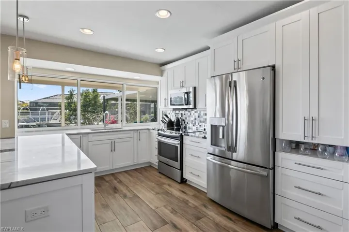 The kitchen features a large, expansive window that frames a breathtaking view of the dock, pool, and shimmering water beyond.