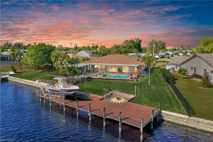 An aerial view of the home reveals a sparkling pool, a serene canal with a boat lift dock, and lush landscaping, creating a peaceful blend of water and outdoor living.