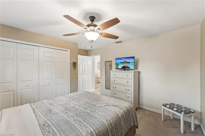 Bedroom with ceiling fan, light colored carpet, and a closet