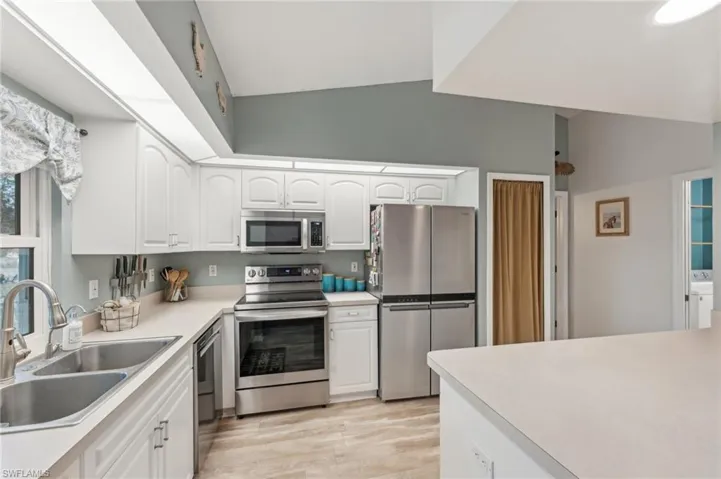 Kitchen featuring stainless steel appliances, sink, light hardwood / wood-style flooring, white cabinets, and lofted ceiling