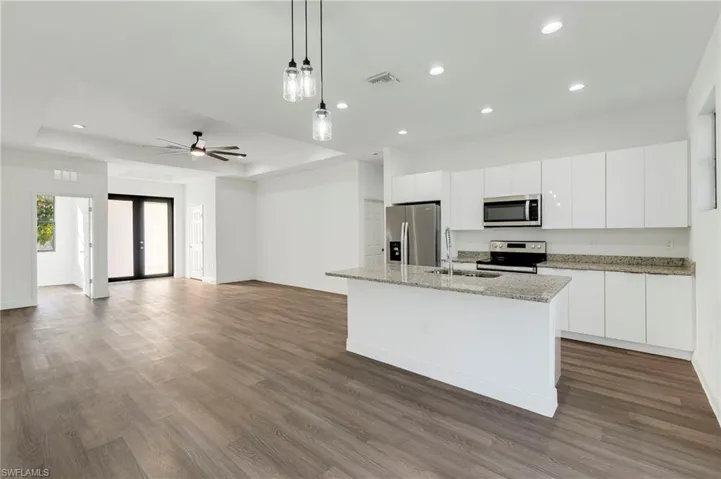Kitchen with appliances with stainless steel finishes, an island with sink, white cabinets, decorative light fixtures, and a raised ceiling