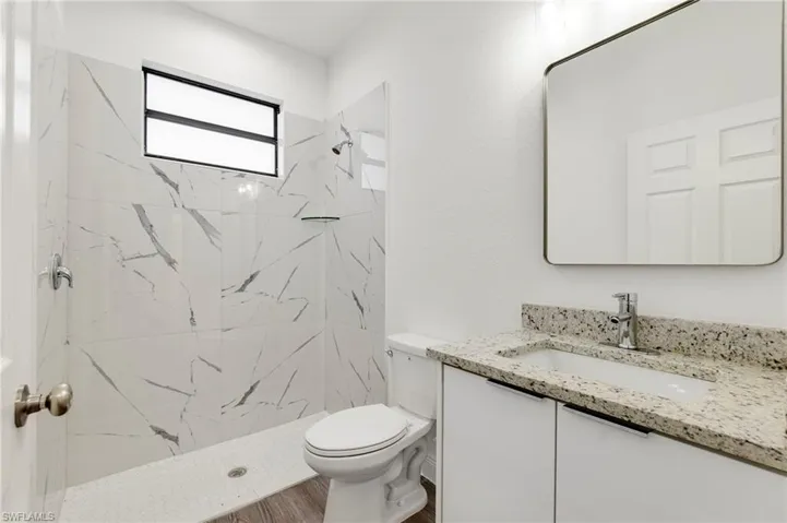 Bathroom featuring vanity, tiled shower, hardwood / wood-style floors, and toilet