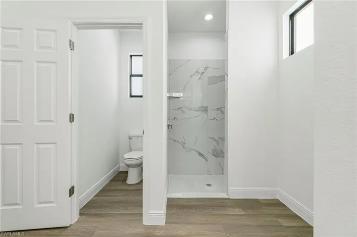 Bathroom featuring hardwood / wood-style floors, toilet, and tiled shower