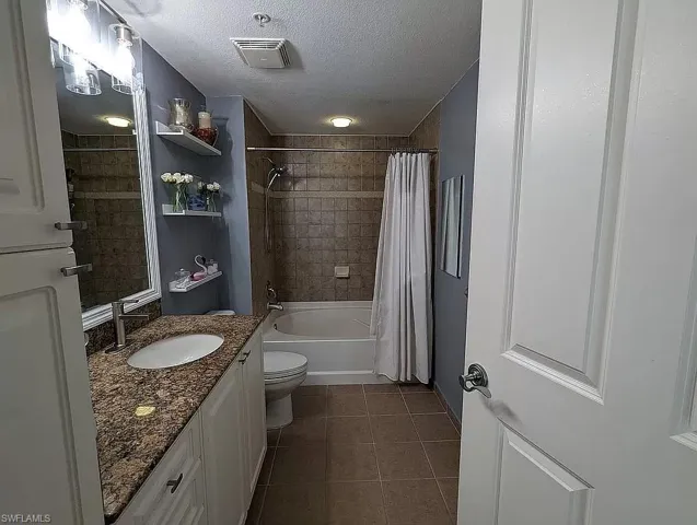 Full bathroom featuring a textured ceiling, toilet, vanity, tile patterned floors, and shower / tub combo