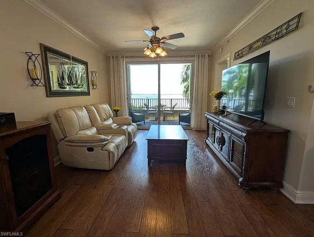Living room with ornamental molding, ceiling fan, and dark wood-type flooring