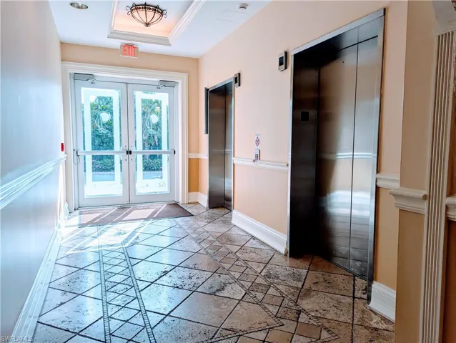 Doorway to outside with tile patterned flooring, a raised ceiling, french doors, and elevator