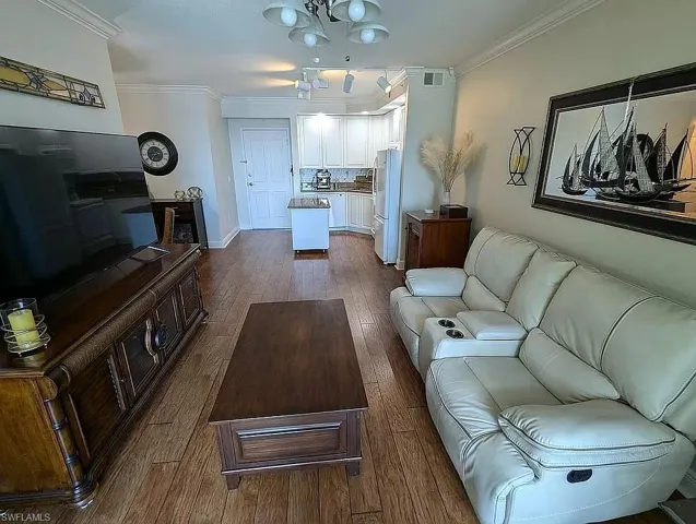 Living room with an inviting chandelier, dark wood-type flooring, and ornamental molding
