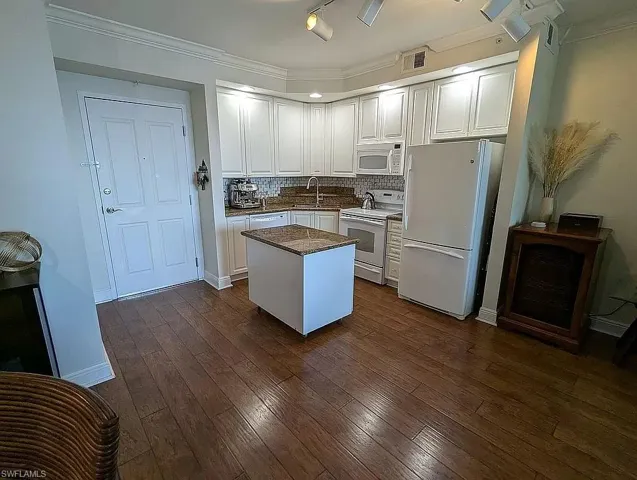 Kitchen with white appliances, white cabinets, dark wood-type flooring, a kitchen island, and sink