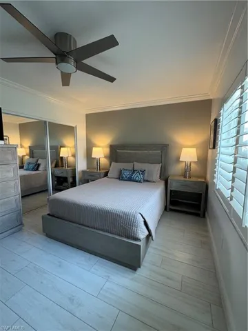 Bedroom with a closet, ornamental molding, light wood-type flooring, and a ceiling fan