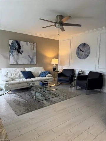 Living room featuring crown molding, a decorative wall, light ceramic tile floors, and ceiling fan