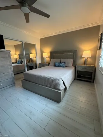 Bedroom with a mirrored closet, light wood-style ceramic flooring, ornamental molding, and ceiling fan