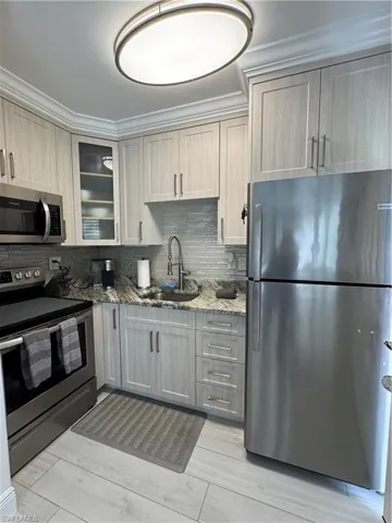 Kitchen with range, stainless steel refrigerator, light stone countertops, glass fronted custom cabinets, and tasteful backsplash