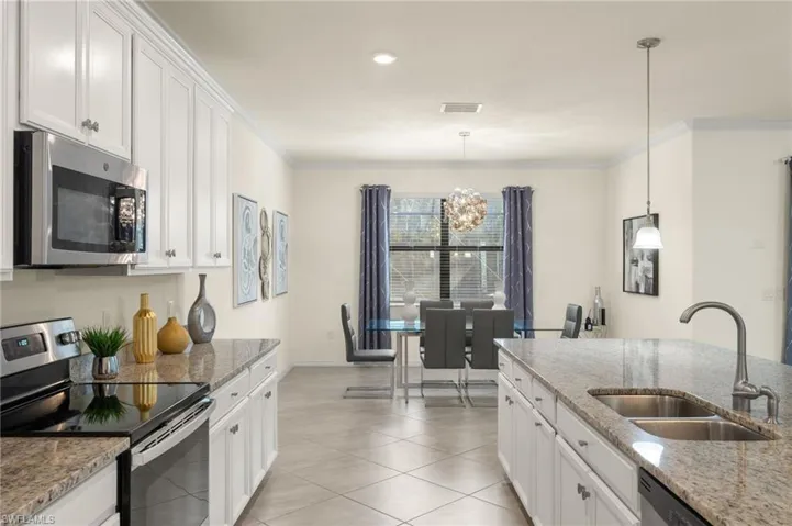 Kitchen with hanging light fixtures, sink, light stone counters, appliances with stainless steel finishes, and white cabinets