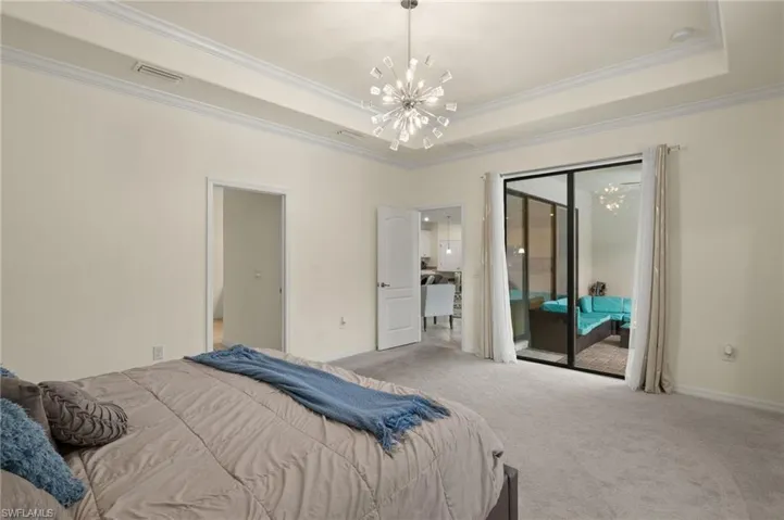 Carpeted bedroom featuring ornamental molding, access to exterior, a chandelier, and a raised ceiling