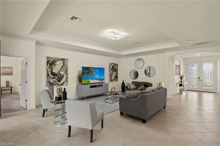 Living room featuring french doors, light tile patterned floors, crown molding, and a raised ceiling