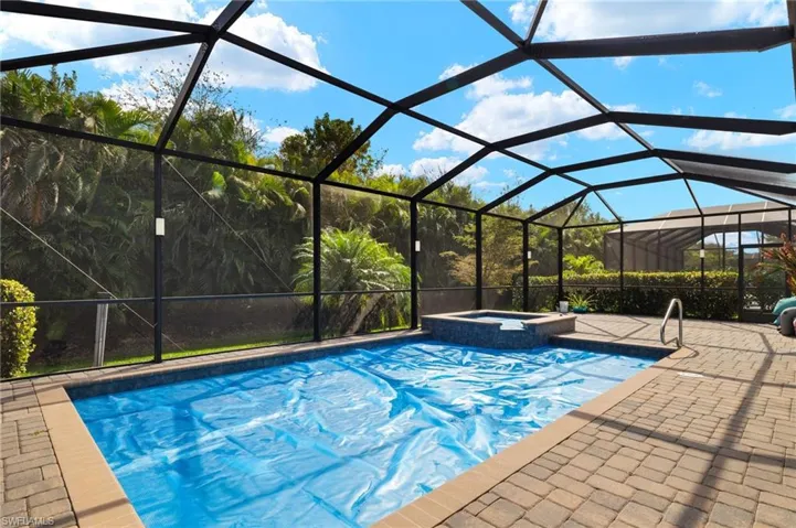 View of swimming pool with an in ground hot tub, glass enclosure, and a patio area