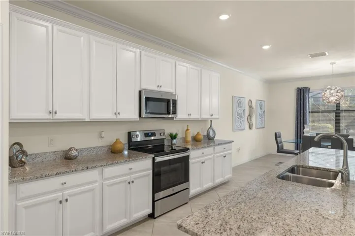 Kitchen with appliances with stainless steel finishes, sink, pendant lighting, white cabinets, and light stone countertops